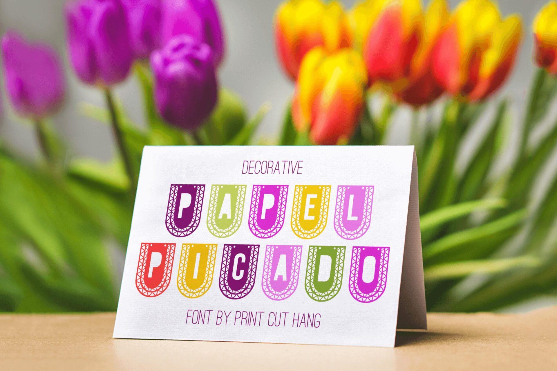 Papel Picado Font by print.cut.hang, letters cut into colorful paper flag shapes on a card preview